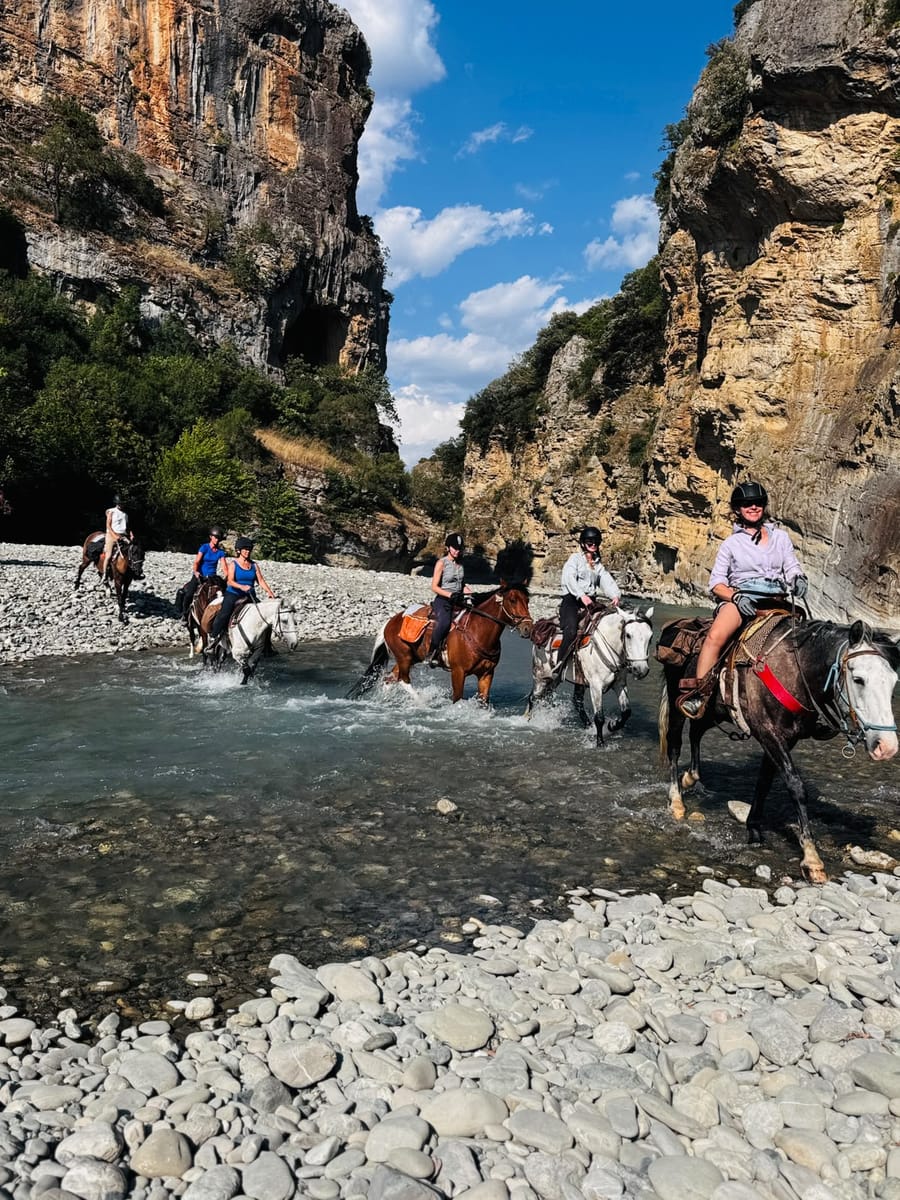 Riders crossing a river at the mouth of a canyon on a horseback riding tour in southern Albania