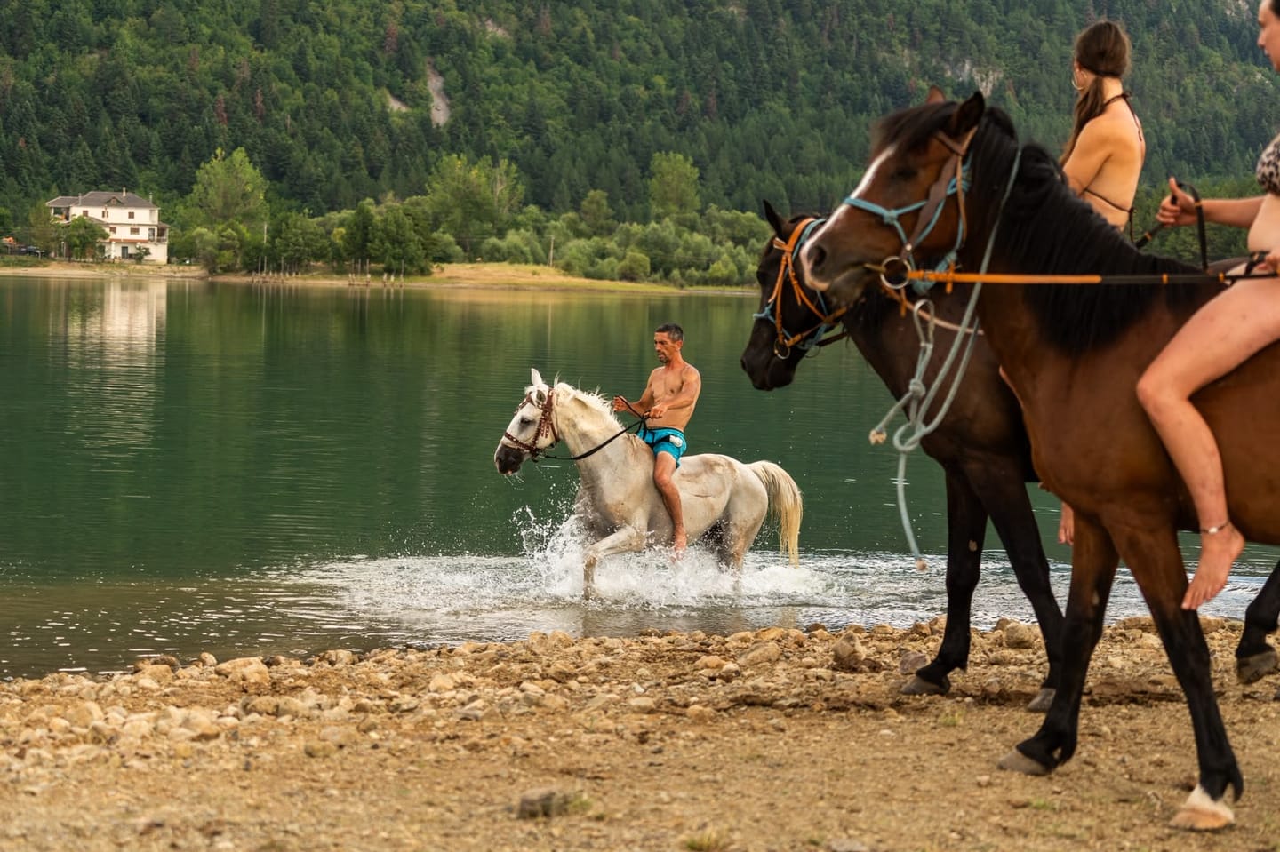 Riders taking their horses into a mountain lake, southern Albania